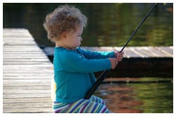 Young child sitting on a dock holding a fishing pole
