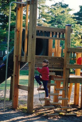 Child on wooden playground rope ladder.