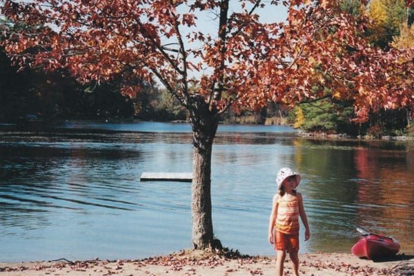 Old photo of young girl on the beach near tree with autumn leaves.