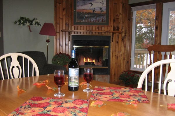 Wine and glasses on dining table, fireplace in background.