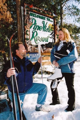 Woman and man posing with Pine Vista Resort sign, ice skates and skis.