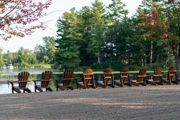 A series of empty beach chairs arranged neatly on the sand, overlooking the lake under a clear blue sky.