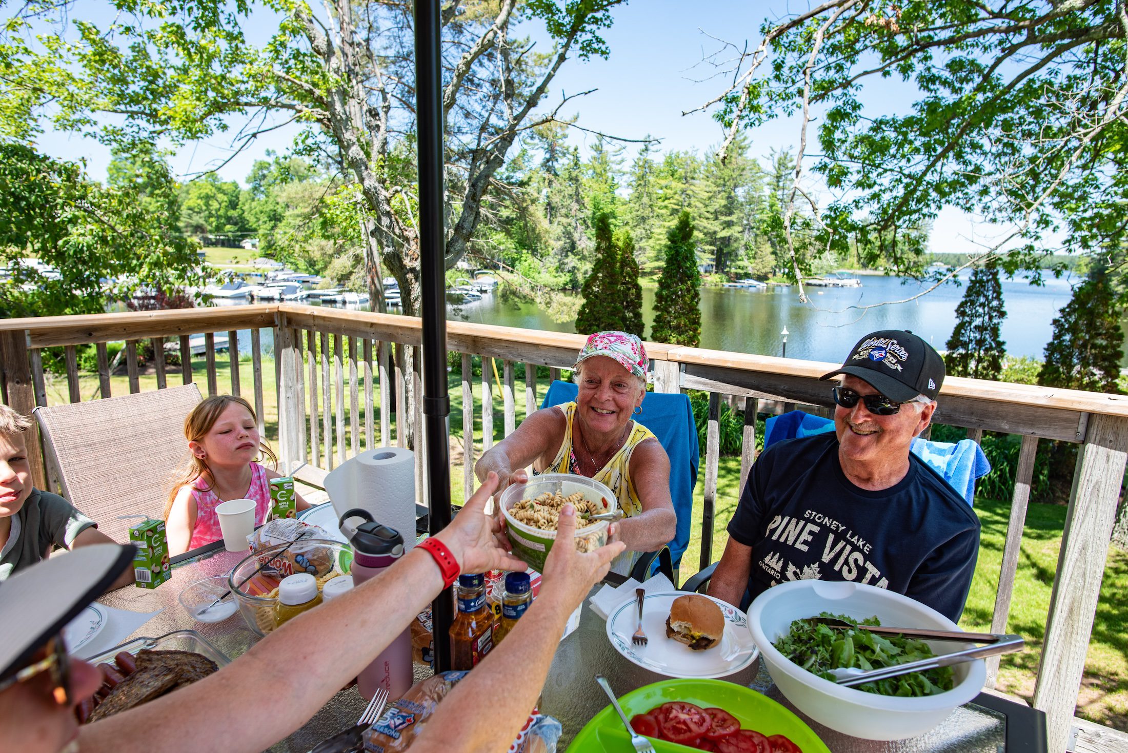 Mike Stiell A group of people pass dishes around a table on a cottage deck