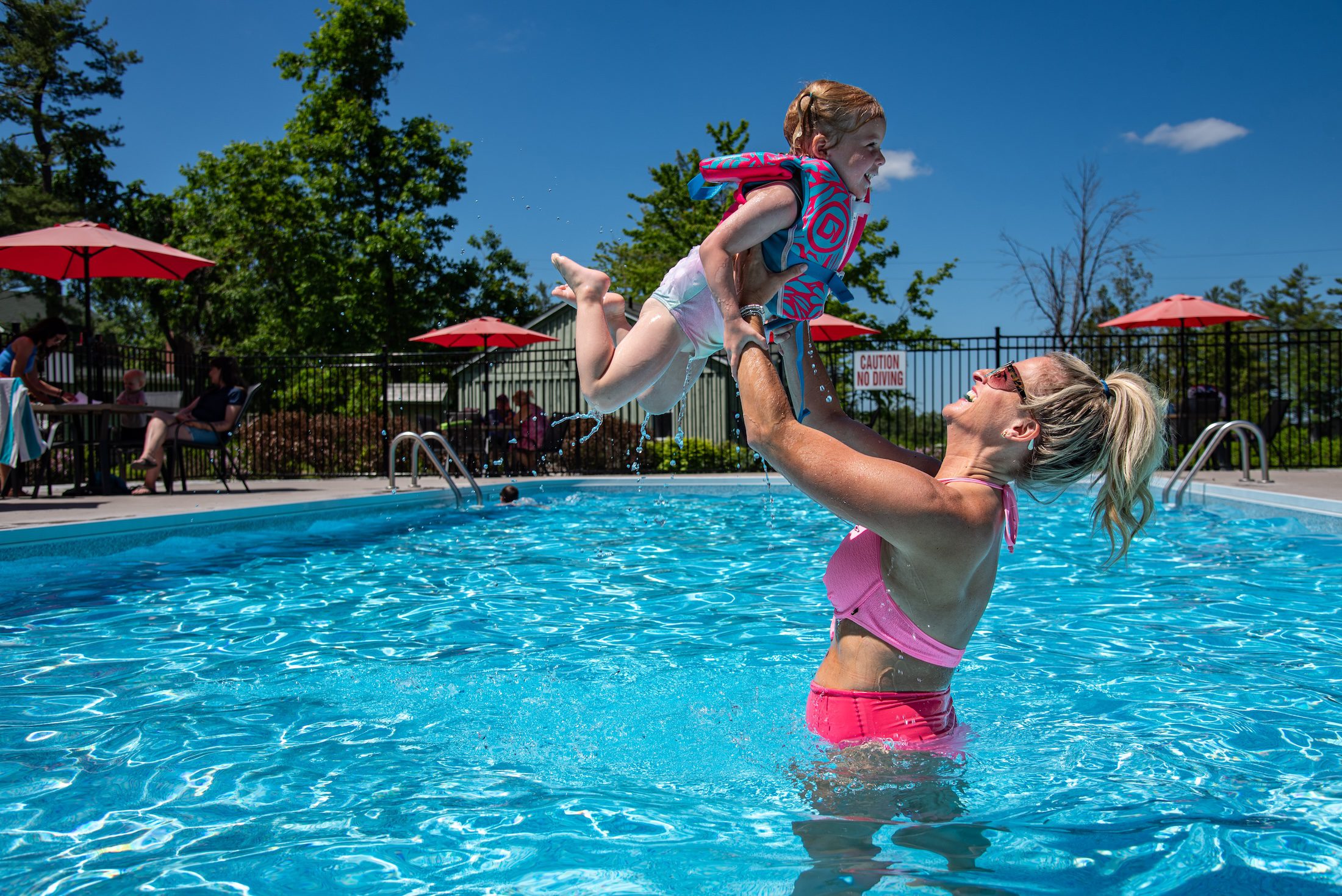 Mike Stiell A woman lifts a child in a jacket jacket into her arms while playing in the pool