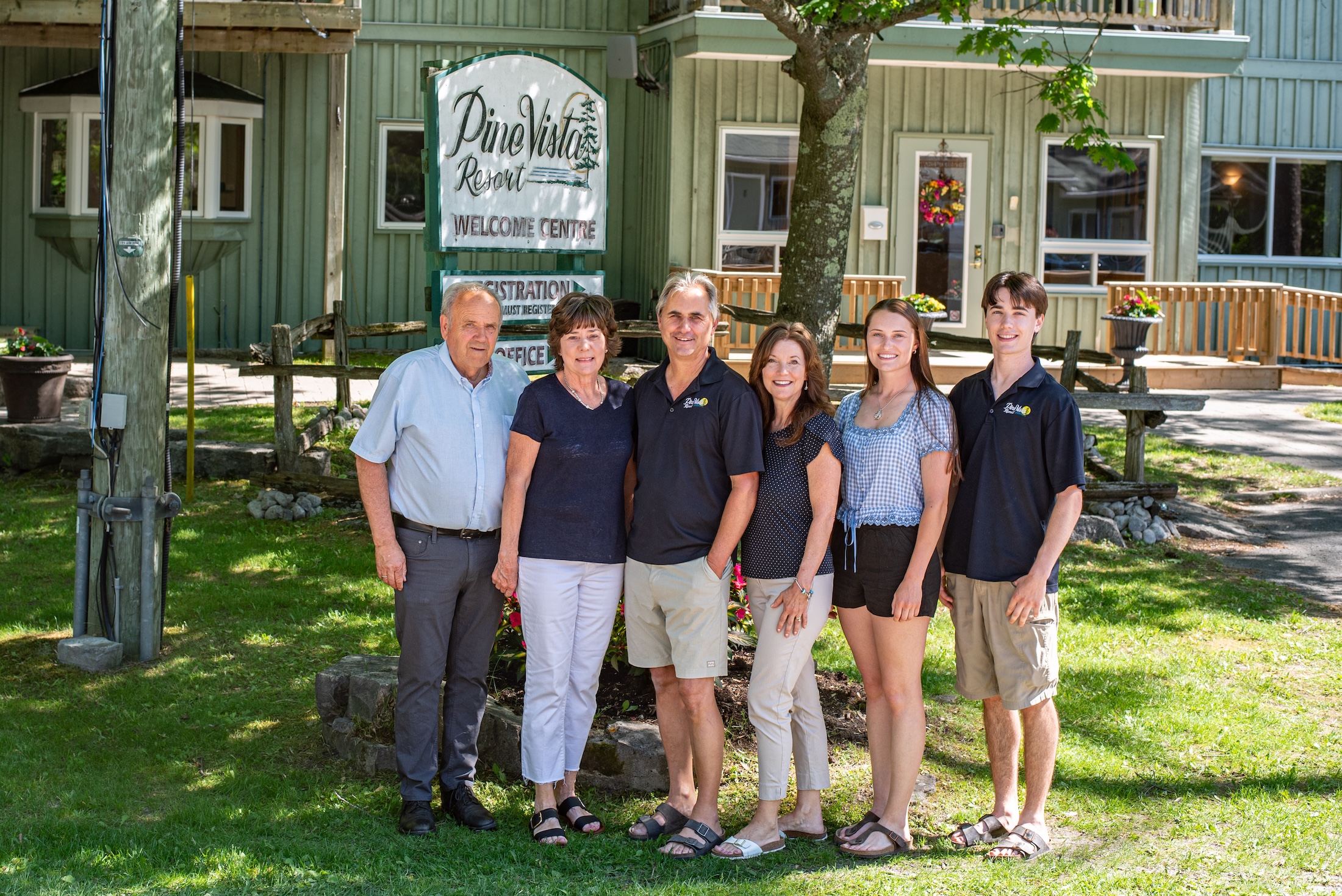 Mike Stiell Six people stand in front of a sign for Pine Vista Resort, posing for a group photo on a sunny day.