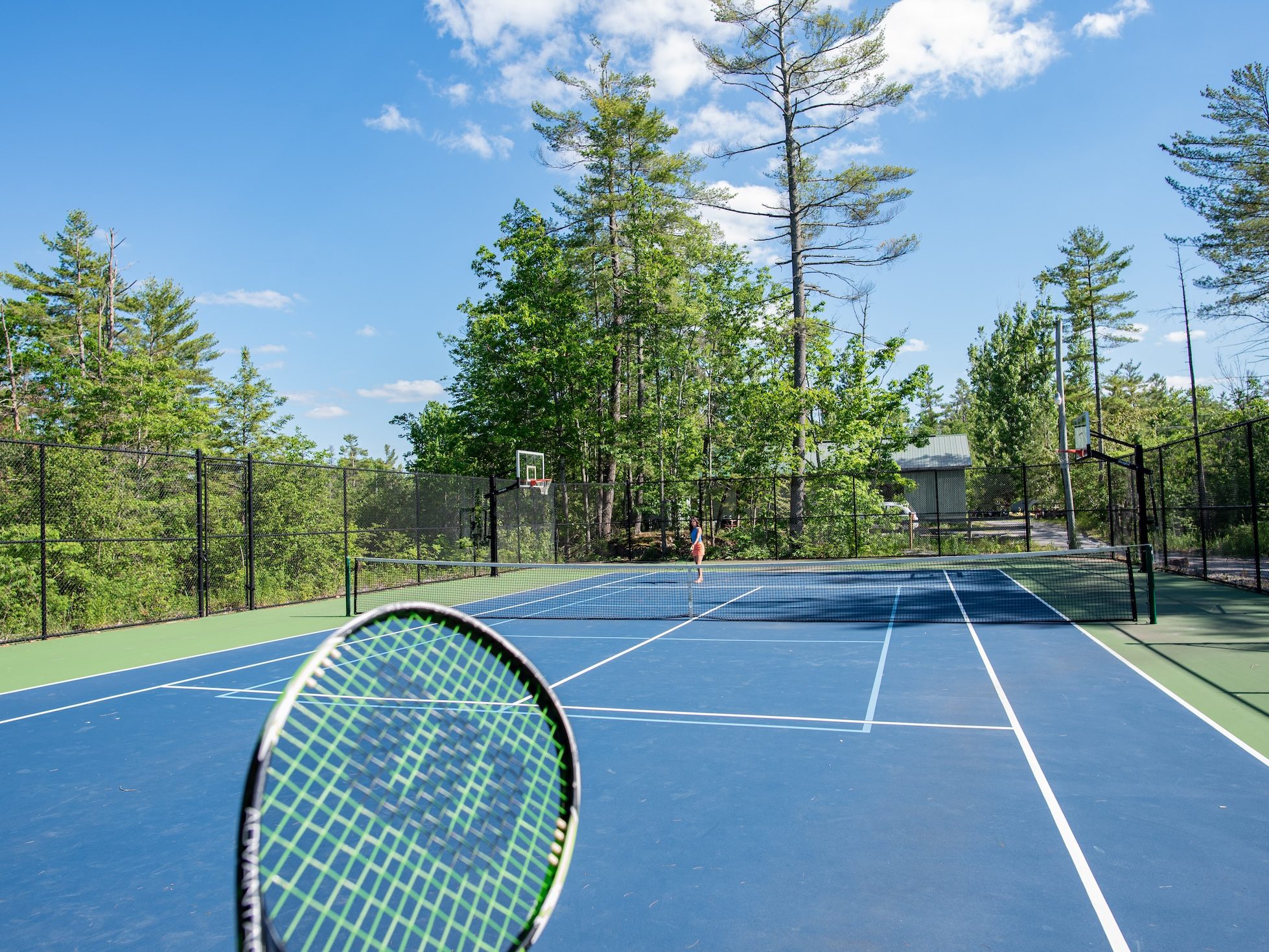 A first-person view of holding a racket and looking down a tennis court