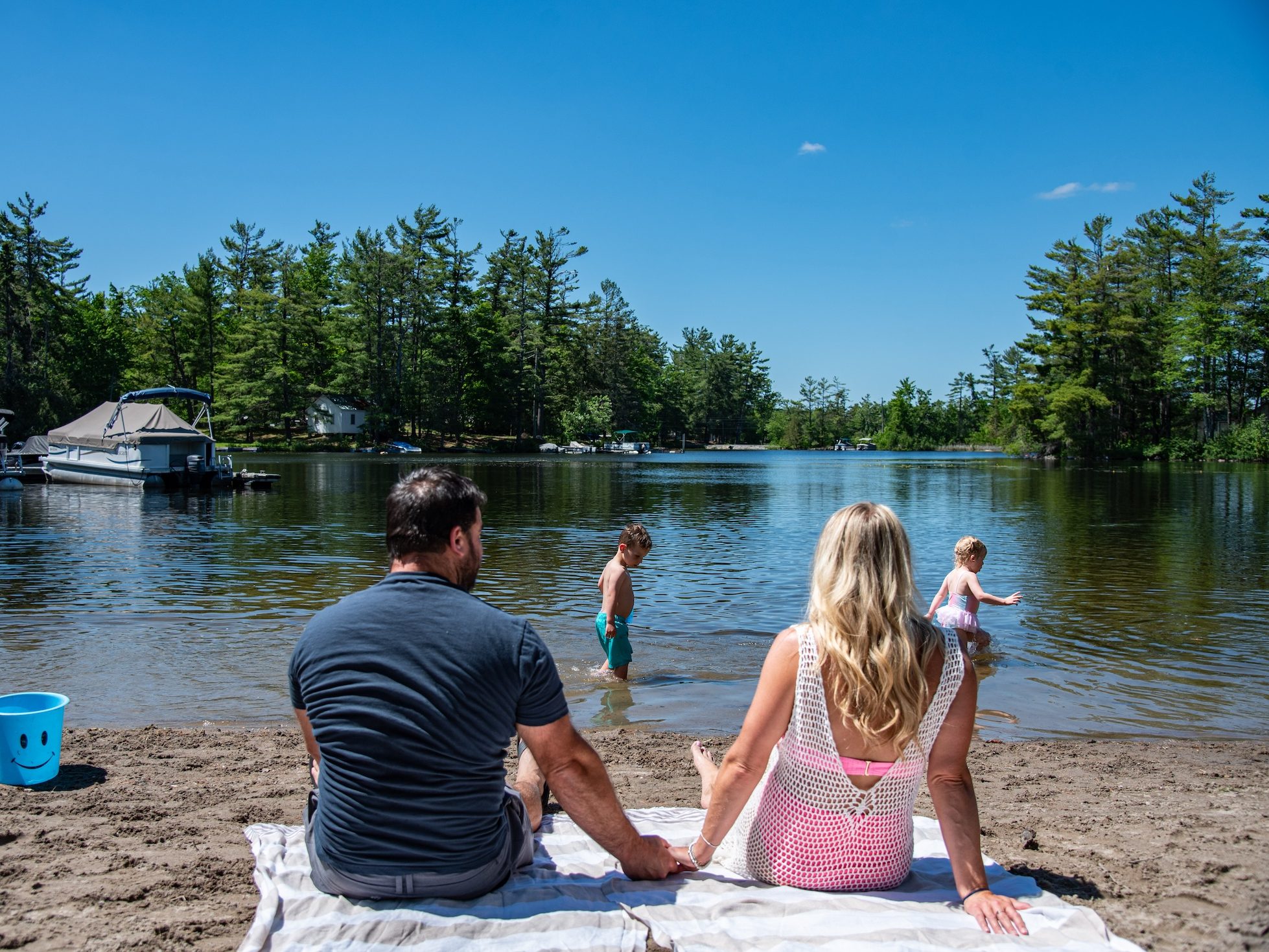 A couple sit on towels by the beach watching children play